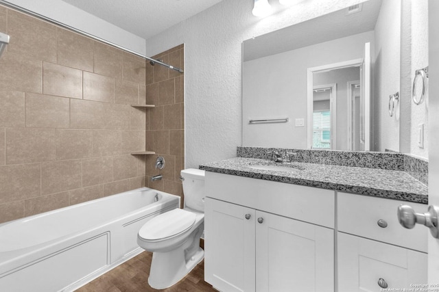 full bathroom featuring toilet, a textured ceiling, vanity, tiled shower / bath combo, and hardwood / wood-style flooring