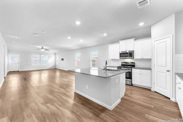 kitchen featuring stone countertops, sink, appliances with stainless steel finishes, white cabinetry, and a center island with sink