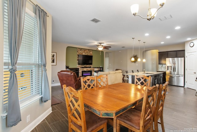 dining area featuring ceiling fan with notable chandelier, a fireplace, and sink