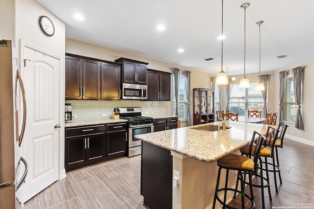 kitchen featuring pendant lighting, a kitchen breakfast bar, a kitchen island with sink, light stone counters, and stainless steel appliances