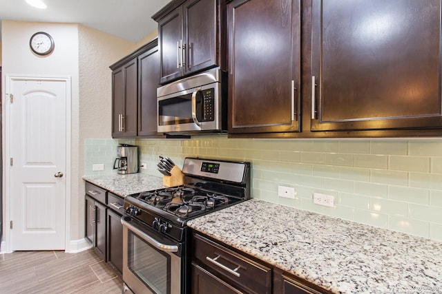 kitchen featuring stainless steel appliances, light stone countertops, backsplash, and dark brown cabinetry