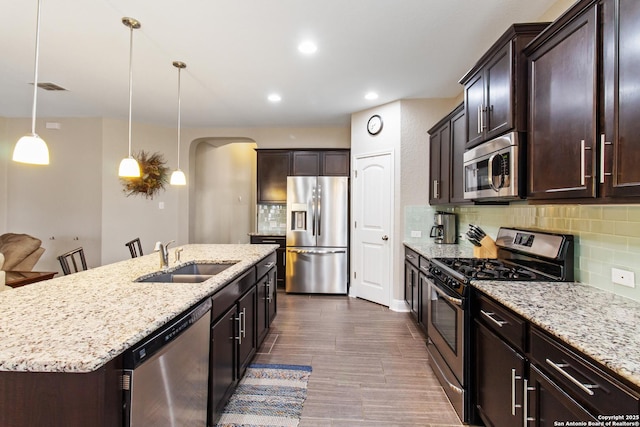 kitchen with pendant lighting, sink, a kitchen island with sink, stainless steel appliances, and a kitchen bar