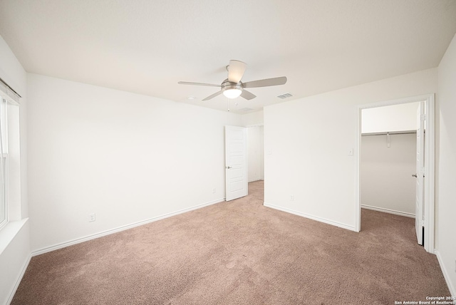 unfurnished bedroom featuring a walk in closet, light colored carpet, a closet, and ceiling fan