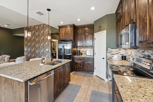 kitchen featuring pendant lighting, an island with sink, sink, backsplash, and stainless steel appliances