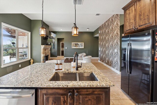 kitchen featuring sink, dishwasher, fridge with ice dispenser, a center island with sink, and a stone fireplace