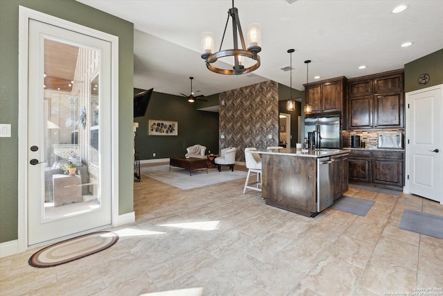 kitchen with a breakfast bar, appliances with stainless steel finishes, a kitchen island with sink, hanging light fixtures, and dark brown cabinets