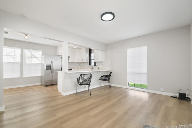 kitchen with a wealth of natural light, kitchen peninsula, white cabinets, a kitchen bar, and stainless steel fridge with ice dispenser