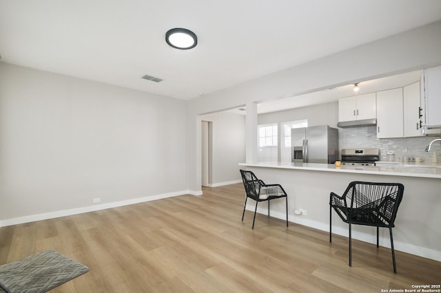 kitchen featuring light hardwood / wood-style flooring, stainless steel appliances, a kitchen breakfast bar, tasteful backsplash, and white cabinets