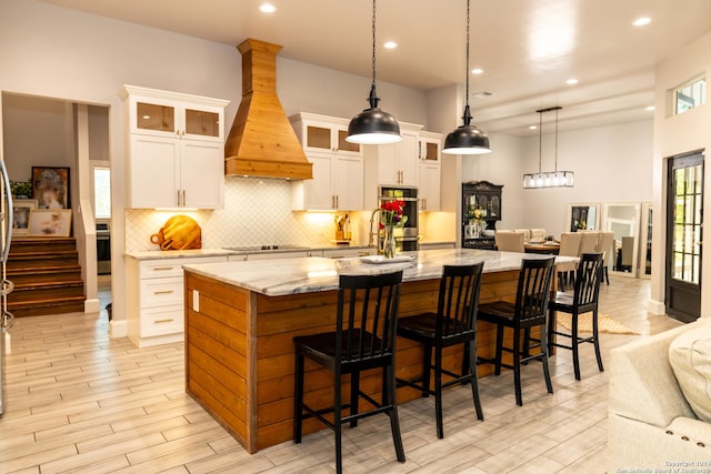 kitchen featuring premium range hood, white cabinets, hanging light fixtures, light stone countertops, and a spacious island