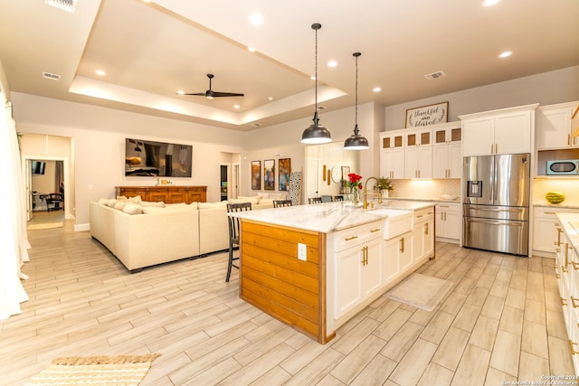 kitchen with sink, a tray ceiling, an island with sink, and stainless steel refrigerator with ice dispenser