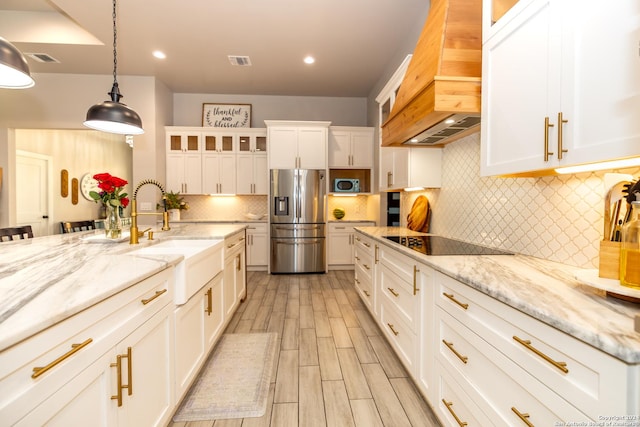 kitchen with premium range hood, decorative light fixtures, white cabinetry, black electric stovetop, and stainless steel refrigerator with ice dispenser