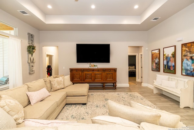 living room with a tray ceiling, a high ceiling, and light wood-type flooring