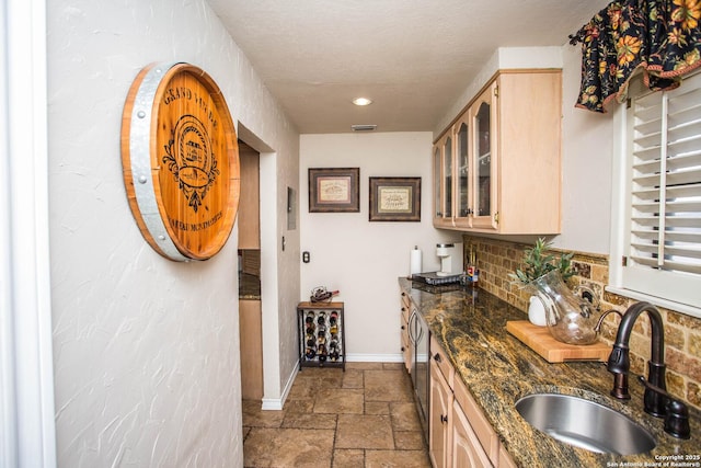 kitchen with sink, tasteful backsplash, a textured ceiling, dark stone countertops, and light brown cabinets