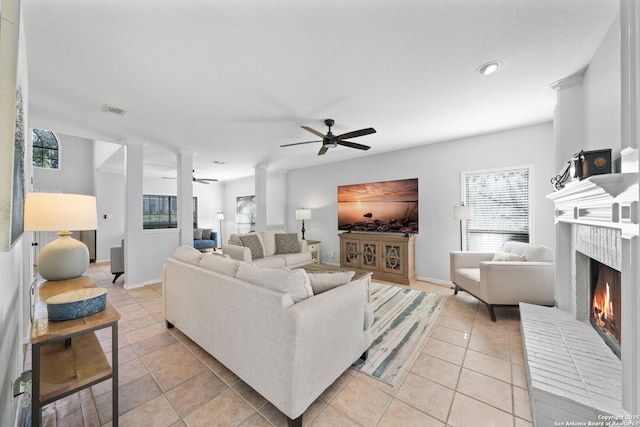 tiled living room with decorative columns, a brick fireplace, and ceiling fan