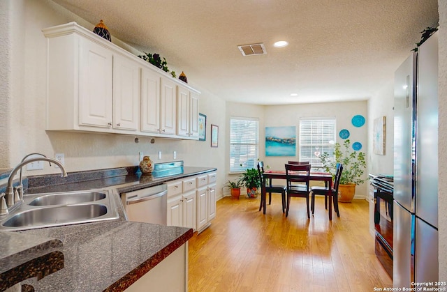 kitchen with appliances with stainless steel finishes, sink, white cabinets, and light wood-type flooring