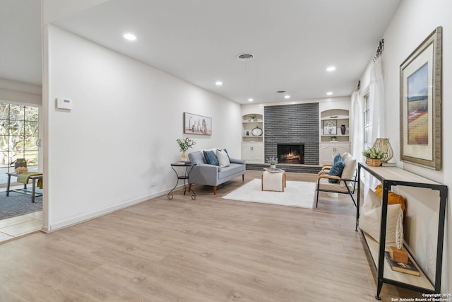 living room with a brick fireplace, light hardwood / wood-style flooring, and built in features