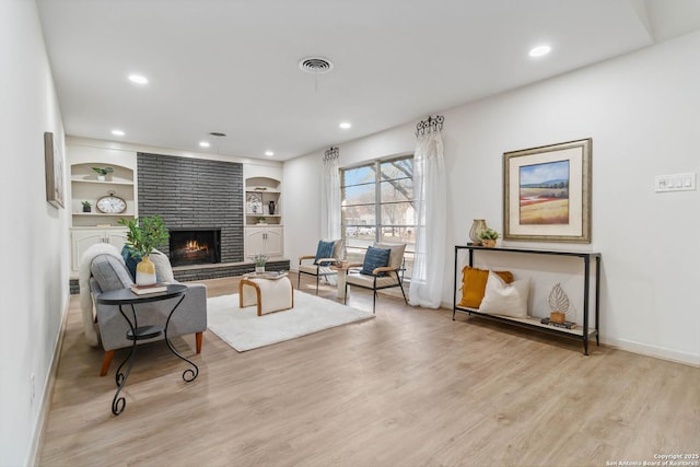 living room featuring a brick fireplace, built in features, and light hardwood / wood-style floors