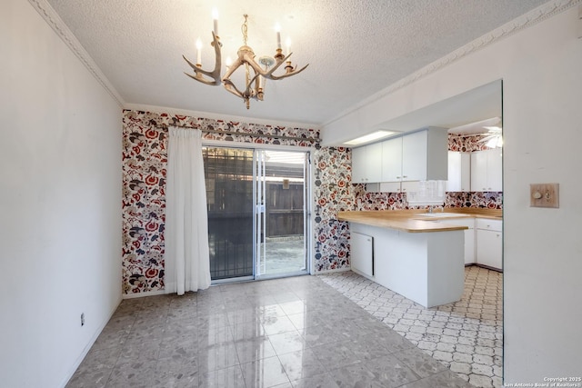 kitchen featuring sink, an inviting chandelier, a textured ceiling, kitchen peninsula, and white cabinets