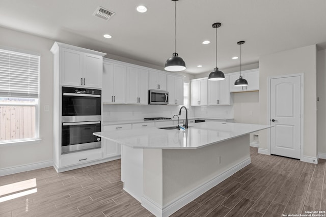 kitchen with pendant lighting, sink, appliances with stainless steel finishes, white cabinets, and a center island with sink