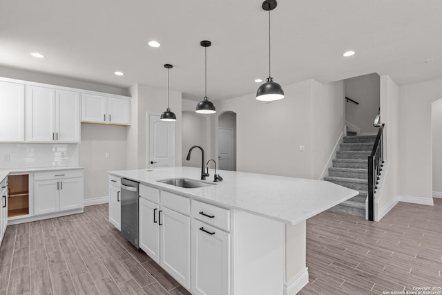 kitchen with decorative light fixtures, sink, white cabinets, light stone counters, and a center island with sink