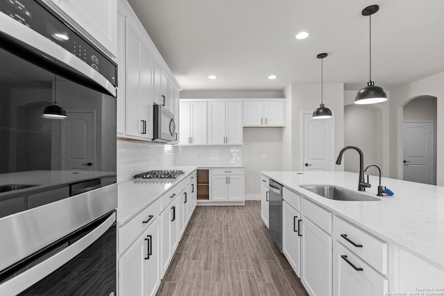 kitchen with sink, pendant lighting, stainless steel appliances, light stone countertops, and white cabinets