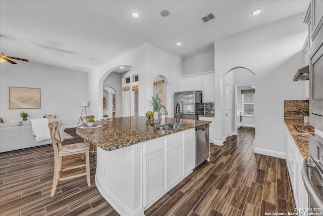 kitchen with sink, appliances with stainless steel finishes, an island with sink, dark stone counters, and white cabinets