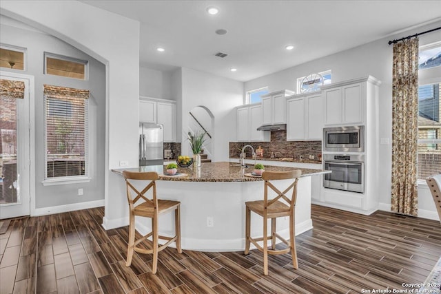 kitchen featuring stone counters, white cabinetry, stainless steel appliances, a kitchen breakfast bar, and decorative backsplash