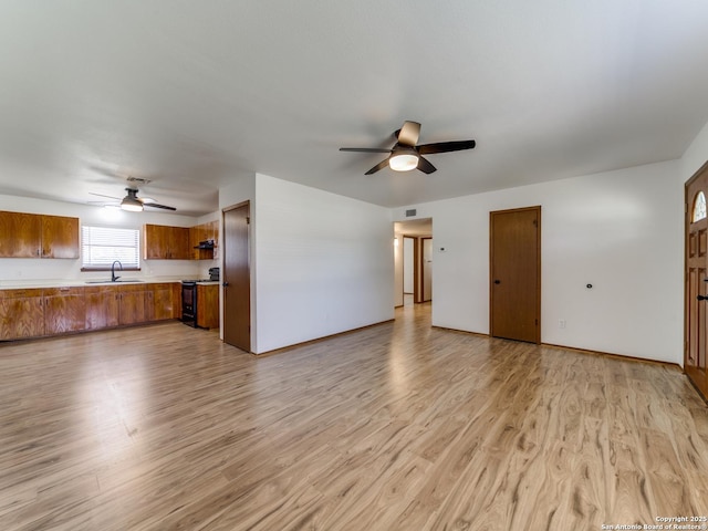 unfurnished living room with a sink, light wood-style floors, and ceiling fan