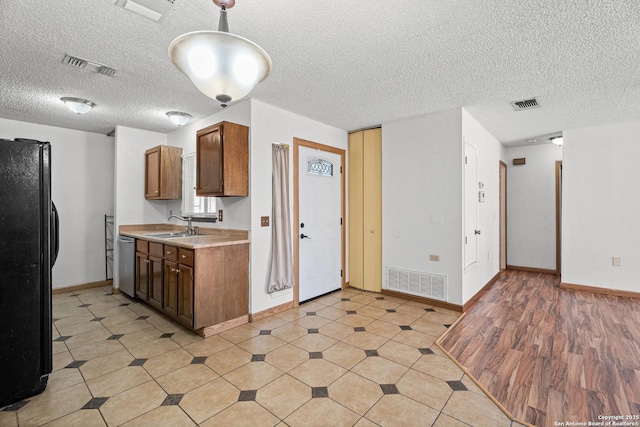 kitchen featuring sink, decorative light fixtures, a textured ceiling, black refrigerator, and dishwasher