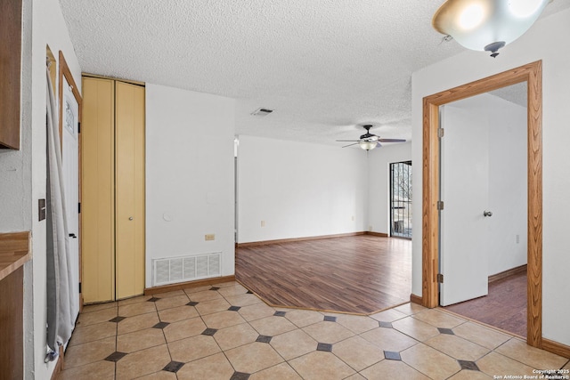 empty room with ceiling fan, light tile patterned floors, and a textured ceiling