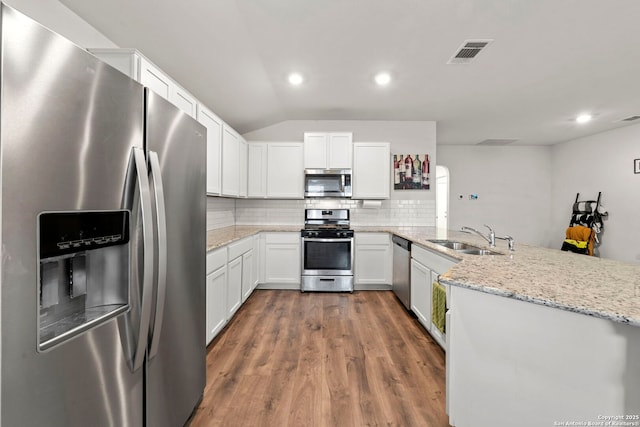 kitchen with white cabinetry, appliances with stainless steel finishes, kitchen peninsula, and light stone counters