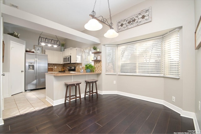 kitchen featuring appliances with stainless steel finishes, pendant lighting, a breakfast bar area, white cabinets, and kitchen peninsula