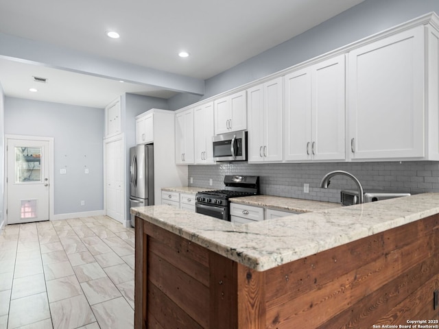 kitchen featuring stainless steel appliances, tasteful backsplash, light stone countertops, white cabinets, and kitchen peninsula