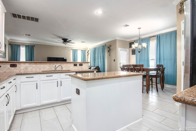 kitchen with a kitchen island, white cabinetry, sink, hanging light fixtures, and ornamental molding