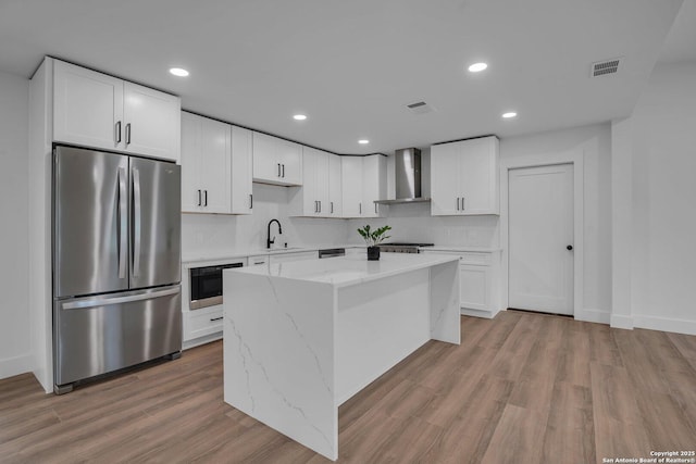 kitchen featuring white cabinets, stainless steel fridge, a kitchen island, and wall chimney range hood