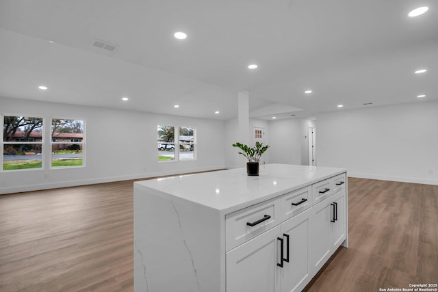 kitchen with white cabinetry, light stone countertops, a center island, and light wood-type flooring