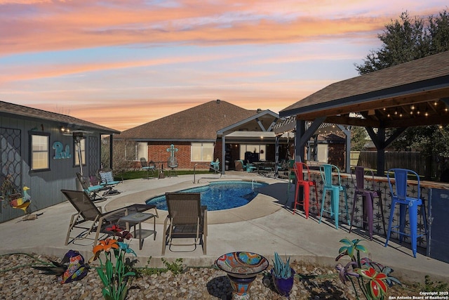 pool at dusk with a gazebo and a patio area