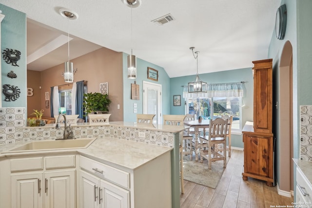 kitchen featuring vaulted ceiling, pendant lighting, sink, decorative backsplash, and kitchen peninsula