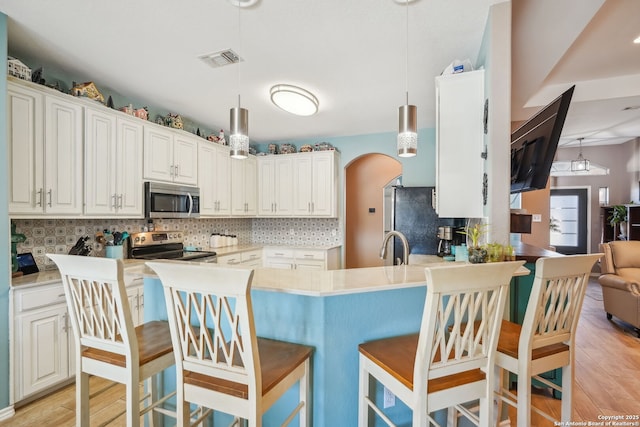 kitchen with stainless steel appliances, pendant lighting, white cabinets, and light wood-type flooring