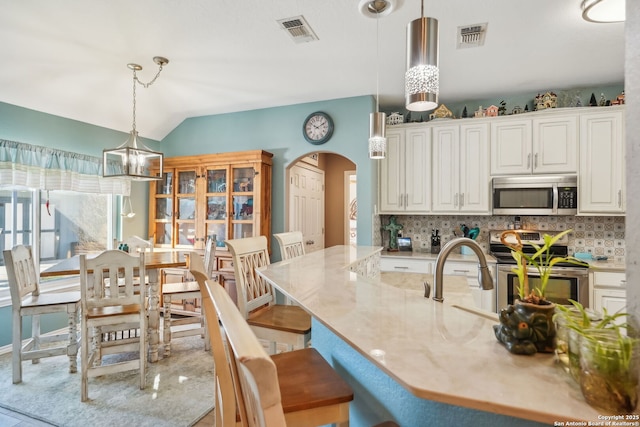 kitchen with decorative light fixtures, vaulted ceiling, stainless steel appliances, and white cabinets