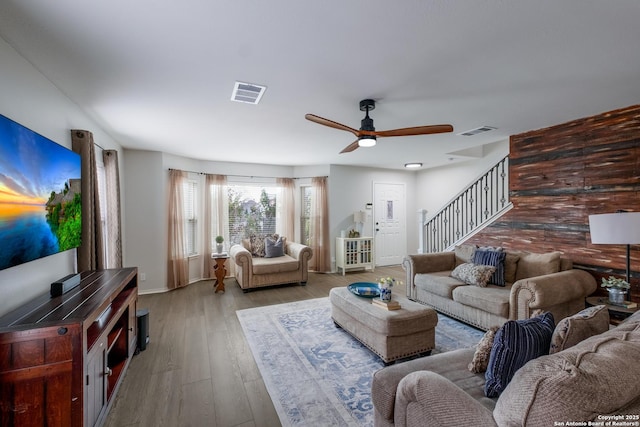 living room with light hardwood / wood-style flooring, wooden walls, and ceiling fan