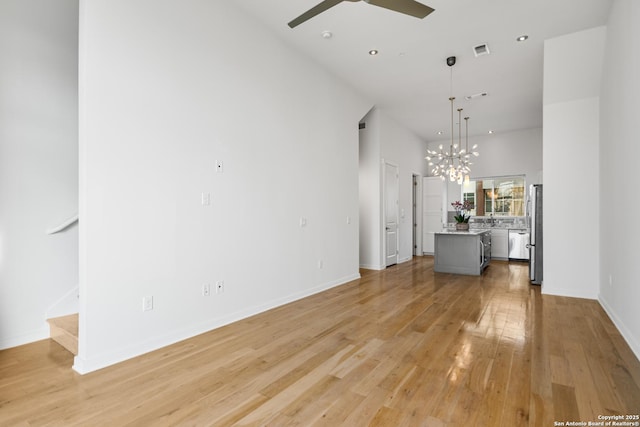 unfurnished living room with baseboards, visible vents, stairs, light wood-type flooring, and ceiling fan with notable chandelier