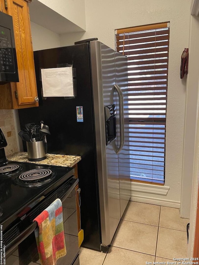 kitchen featuring tasteful backsplash, light tile patterned floors, light stone counters, and black appliances