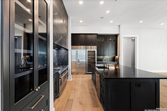 kitchen with high end appliances, sink, light hardwood / wood-style floors, and an island with sink