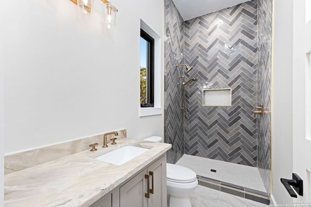 bathroom featuring a tile shower, vanity, and toilet