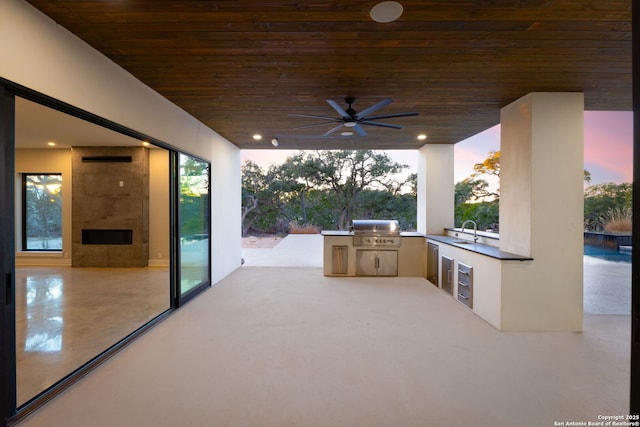 patio terrace at dusk with ceiling fan, area for grilling, exterior kitchen, and sink