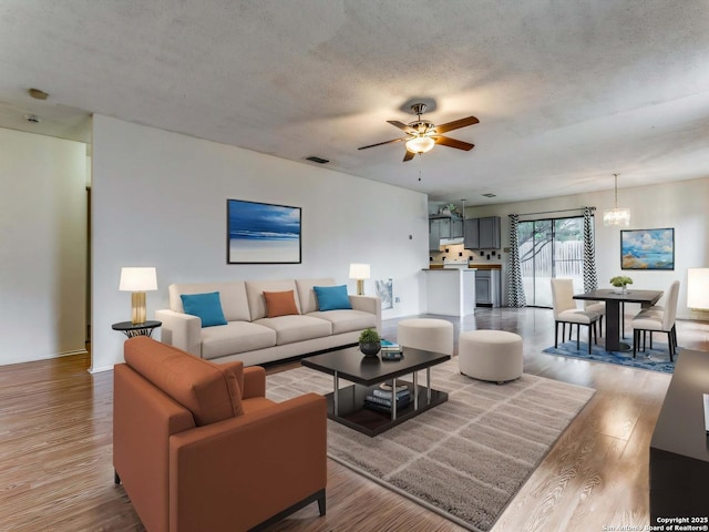 living room with hardwood / wood-style flooring, ceiling fan with notable chandelier, and a textured ceiling