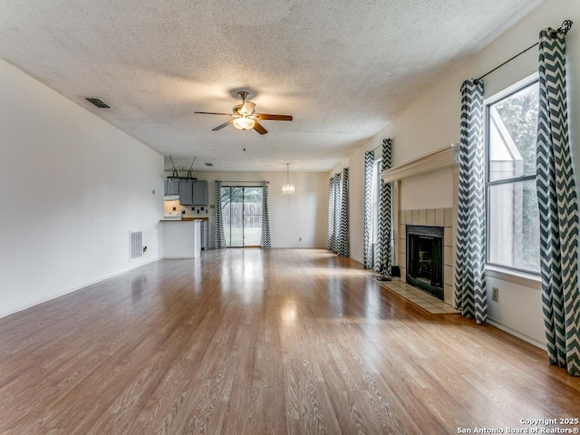 unfurnished living room with a textured ceiling, a tile fireplace, light hardwood / wood-style floors, and ceiling fan