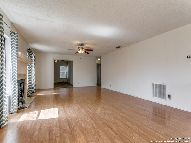 unfurnished living room featuring ceiling fan, a textured ceiling, a fireplace, and light wood-type flooring