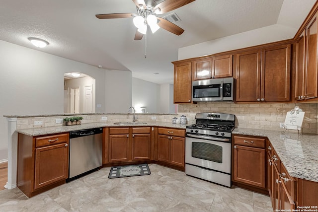 kitchen featuring sink, light stone countertops, kitchen peninsula, and appliances with stainless steel finishes